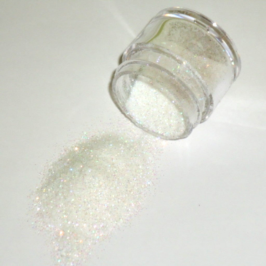Small clear jar tipped on its side spilling rainbow glitter dust onto a white surface, with fine iridescent particles reflecting soft multicolor sparkle.