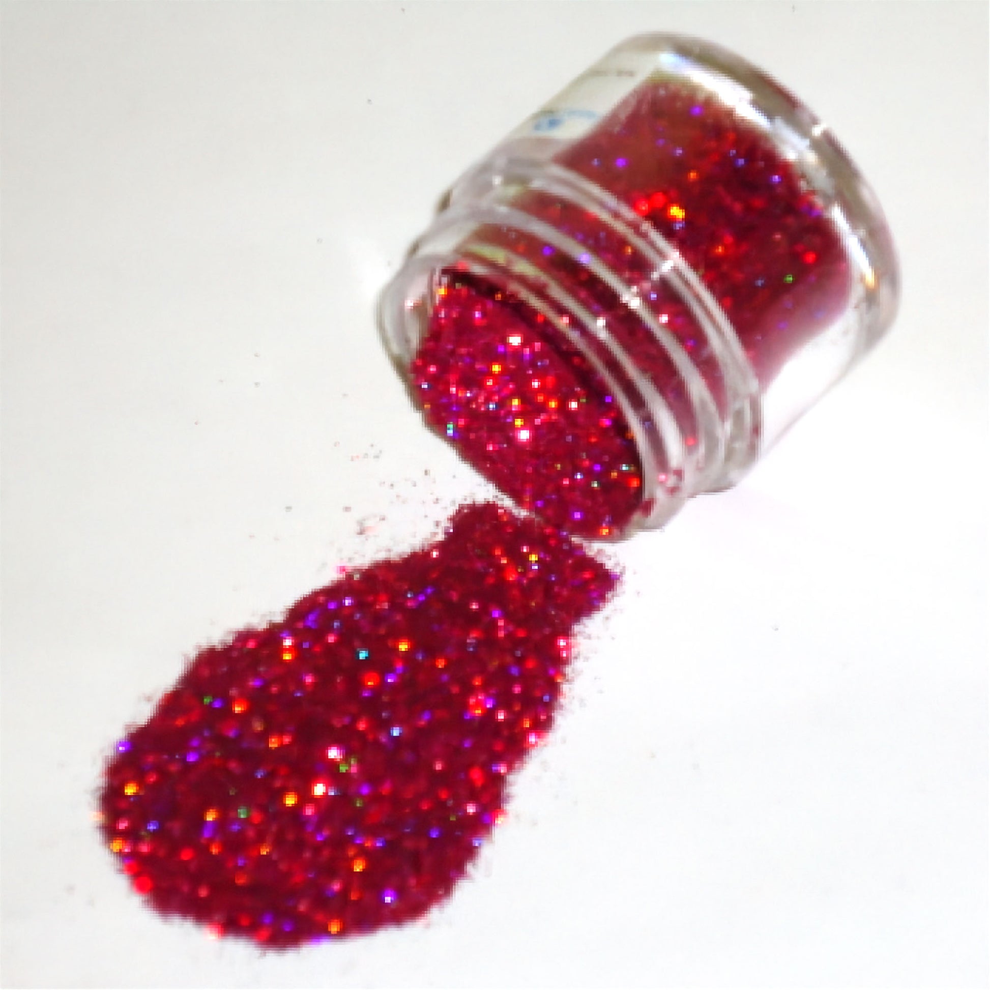 Clear plastic jar tipped on its side spilling bright raspberry red glitter dust onto a white surface, with multi-color reflective sparkles visible in the pile.