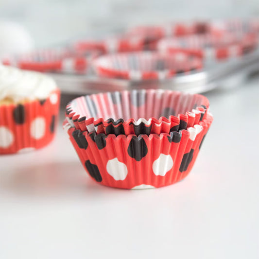 Red, black, and white polka dot baking cups stacked inside a muffin tin with cupcakes in the background.