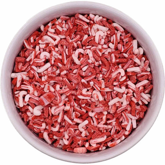 Top-down view of a round container filled with red and white candy cane–shaped sprinkles, showing a textured mix of crushed peppermint candy pieces