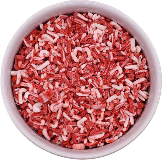 Top-down view of a round container filled with red and white candy cane–shaped sprinkles, showing a textured mix of crushed peppermint candy pieces