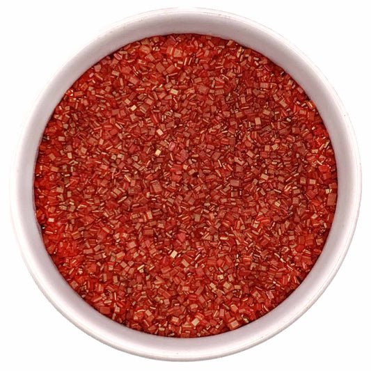 Top-down view of a white bowl filled with red coarse sanding sugar crystals, showing chunky sparkling granules in a bright cherry-red color.