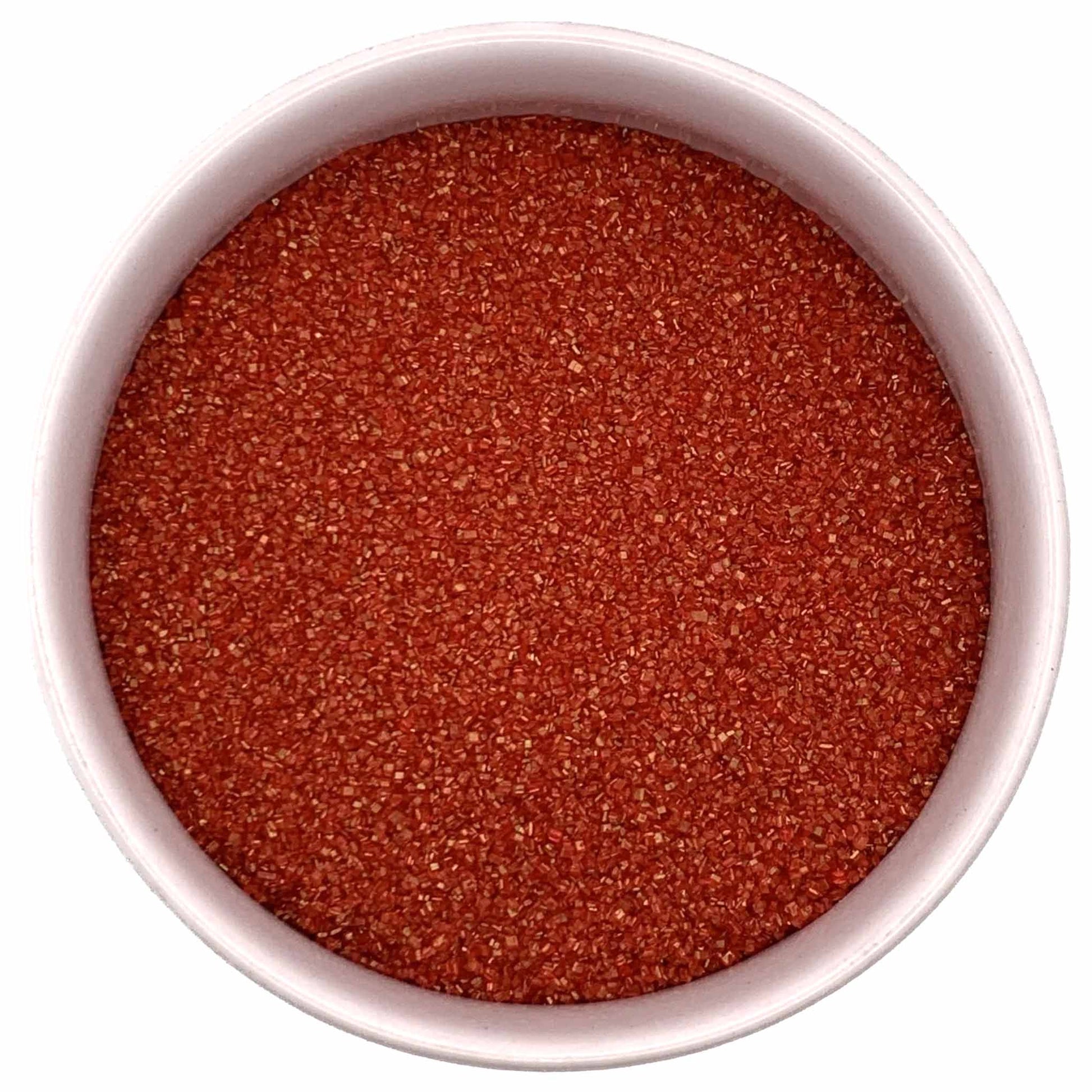 Top-down view of a white bowl filled with red fine sanding sugar, showing tiny sparkling crystals in a bright festive red shade.
