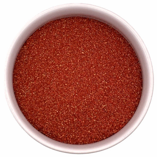 Top-down view of a white bowl filled with red fine sanding sugar, showing tiny sparkling crystals in a bright festive red shade.