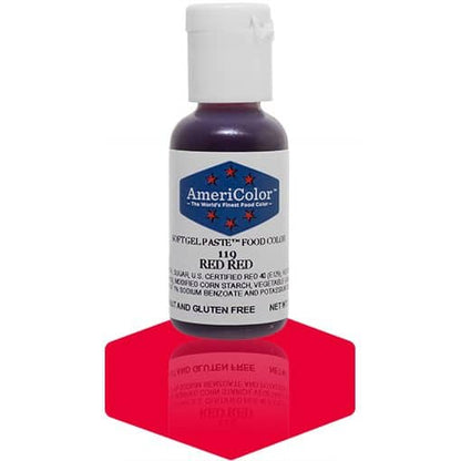 A bottle of AmeriColor Red Red soft gel paste food coloring with a white cap, blue label, and red stars, standing on a deep red reflective surface that mirrors the bottle.