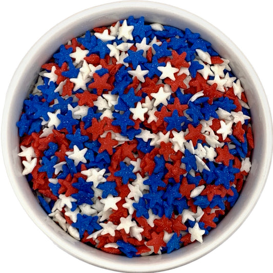 Top-down view of a white bowl filled with small red, white, and blue star-shaped sprinkles clustered together.