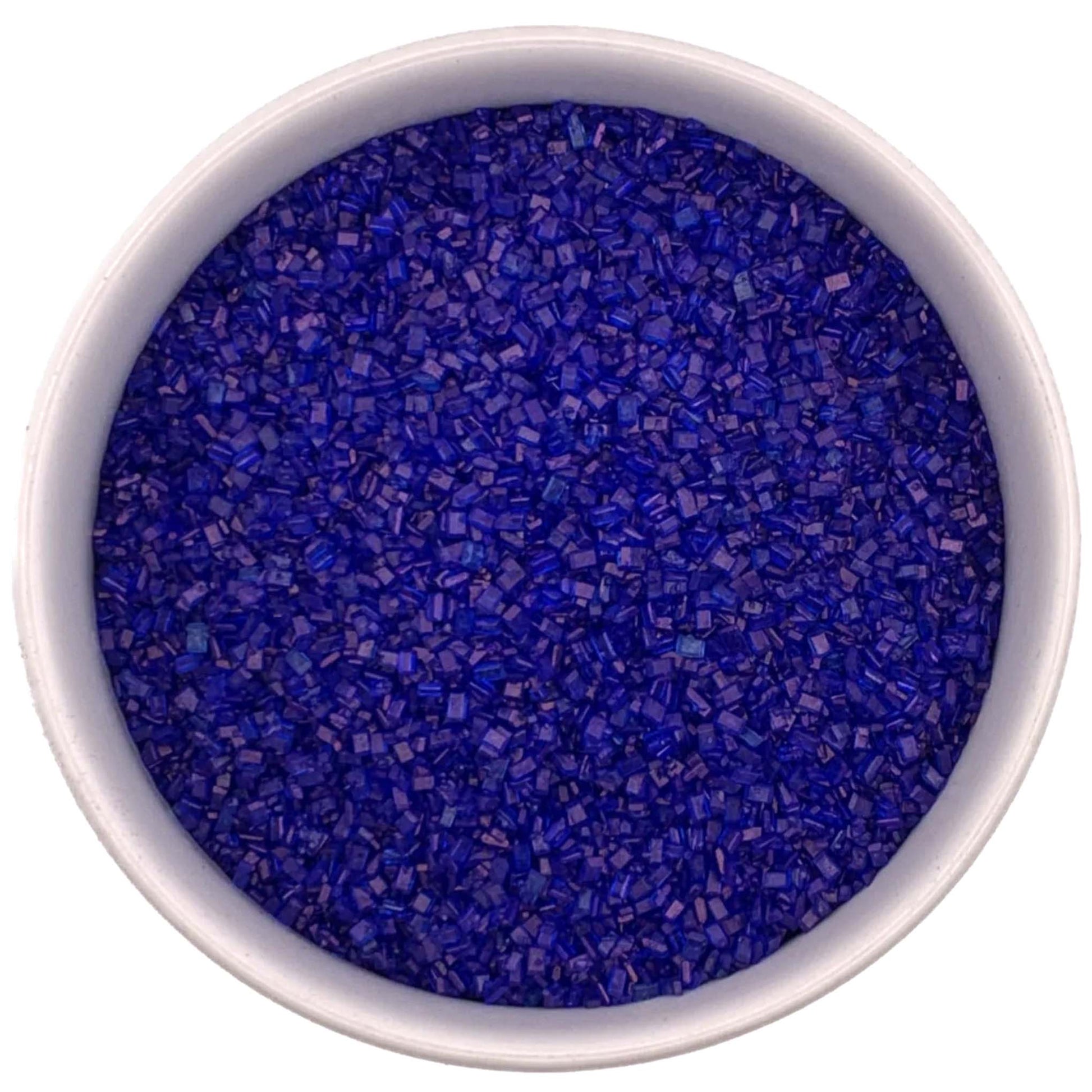 Top-down view of a white bowl filled with royal blue coarse sanding sugar crystals, showing chunky sparkling granules in a deep vivid blue color.