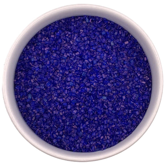 Top-down view of a white bowl filled with royal blue coarse sanding sugar crystals, showing chunky sparkling granules in a deep vivid blue color.