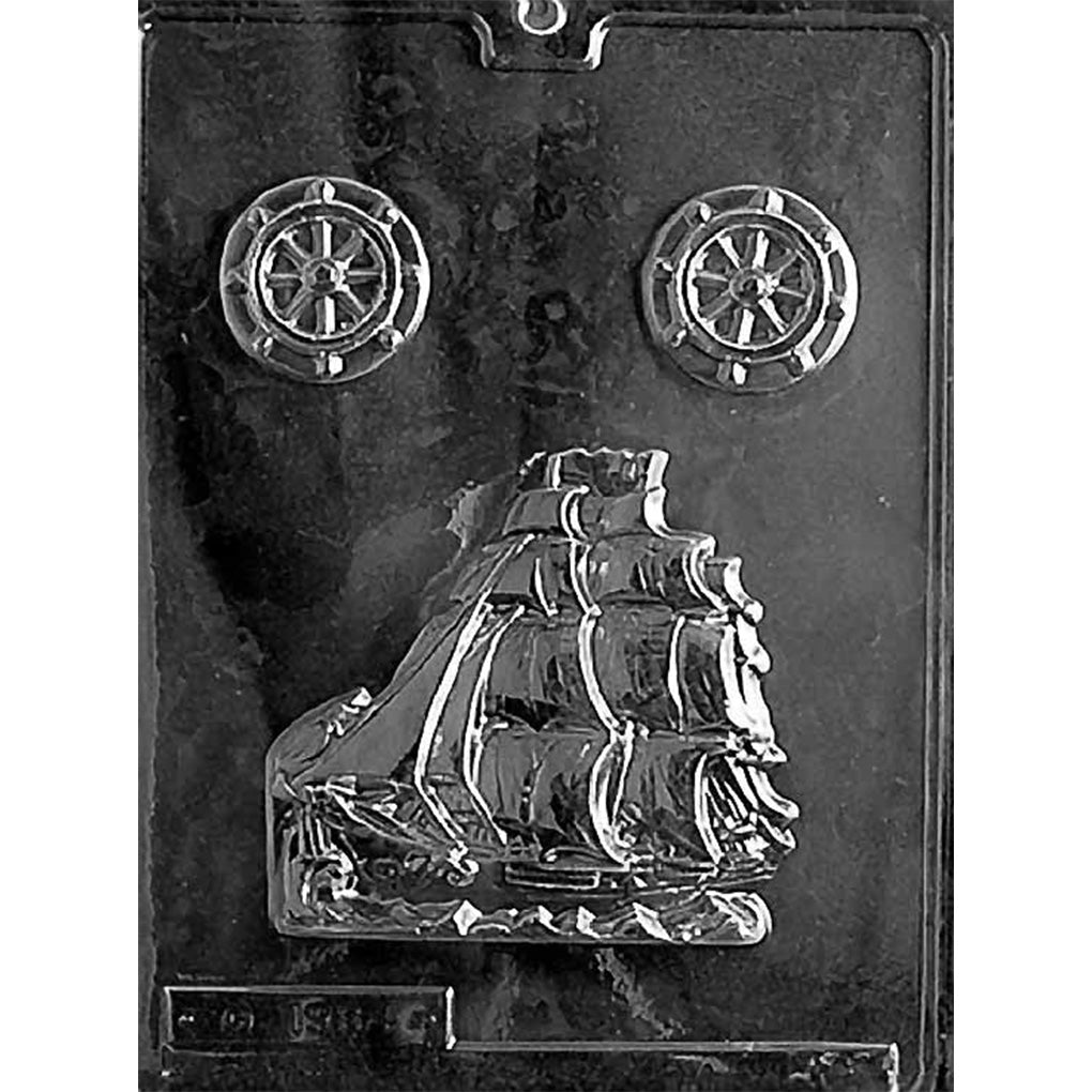 Clear plastic chocolate mold photographed on a dark background with one large sailing schooner cavity showing a tall ship with multiple sails, plus two small round ship wheel cavities near the top.