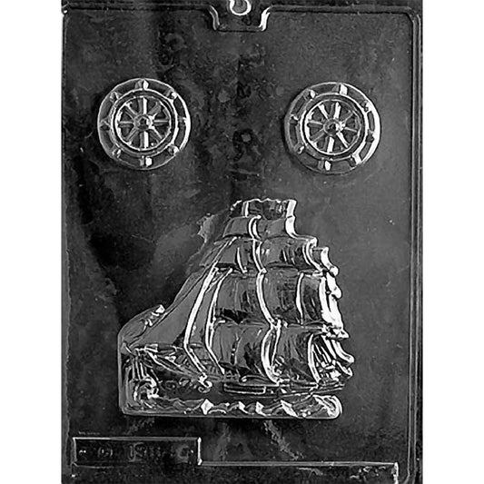 Clear plastic chocolate mold photographed on a dark background with one large sailing schooner cavity showing a tall ship with multiple sails, plus two small round ship wheel cavities near the top.