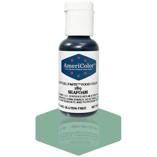A bottle of AmeriColor Seafoam soft gel paste food coloring, showcasing a white cap and blue label with red stars, placed on a shiny seafoam surface that reflects the bottle.