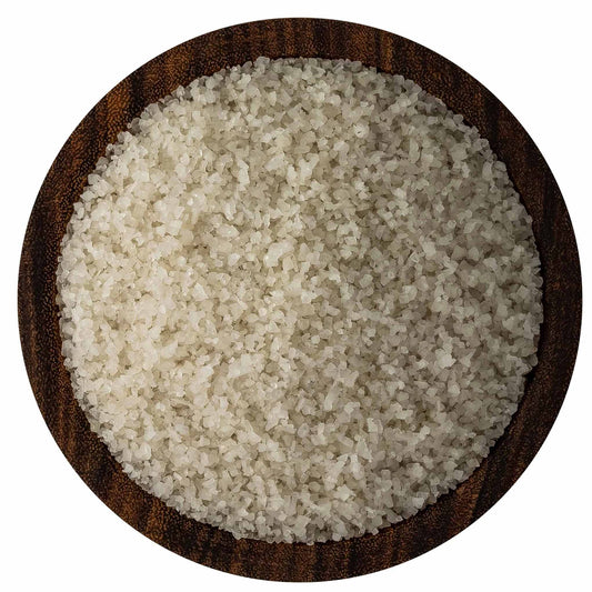 Overhead view of fine French grey sea salt crystals in a round dark wooden bowl on a white background, showing pale grey-beige grains.