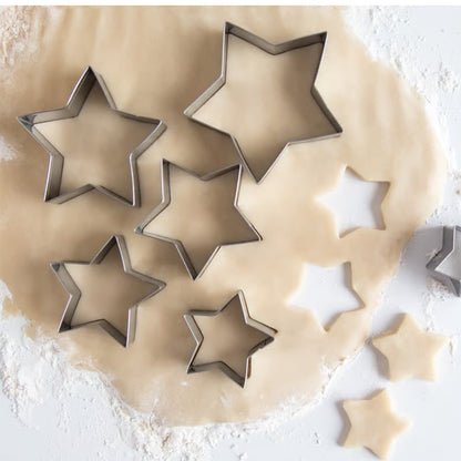 Various sizes of star cookie cutters placed on rolled-out dough, with star-shaped cutouts visible.