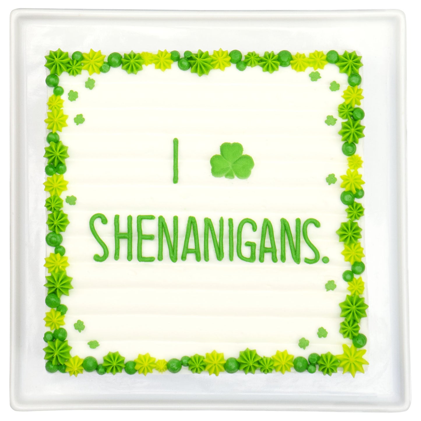 Rectangular sheet cake with a green piped border and small shamrock accents, featuring the word “SHENANIGANS” in green icing on a white background.