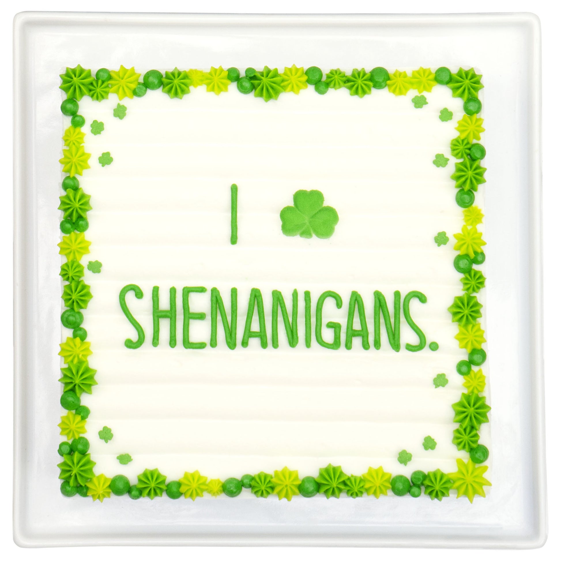 Rectangular sheet cake with a green piped border and small shamrock accents, featuring the word “SHENANIGANS” in green icing on a white background.