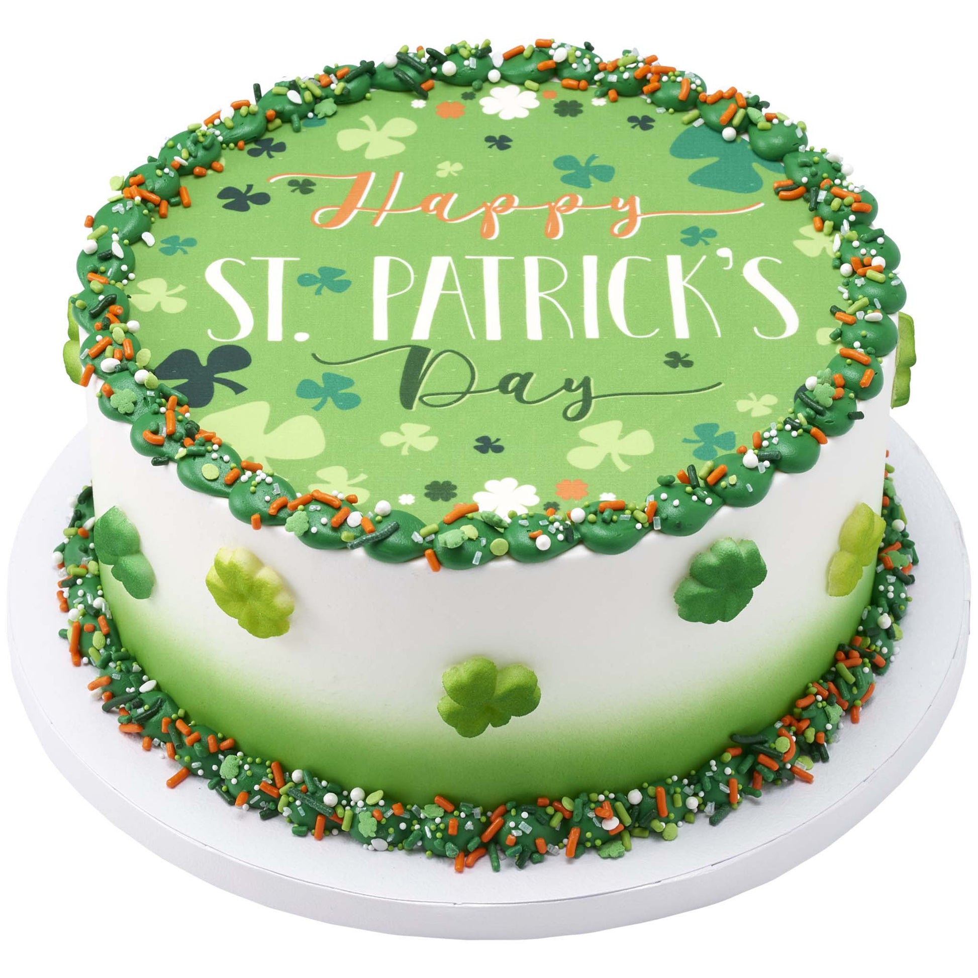 Round cake with green frosting border and a “Happy St. Patrick’s Day” printed topper, decorated with shamrock accents and mixed green-orange-white sprinkles.