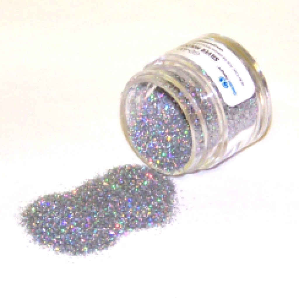Small clear jar tipped on its side spilling silver hologram glitter dust onto a white surface, with fine sparkling particles reflecting rainbow highlights.