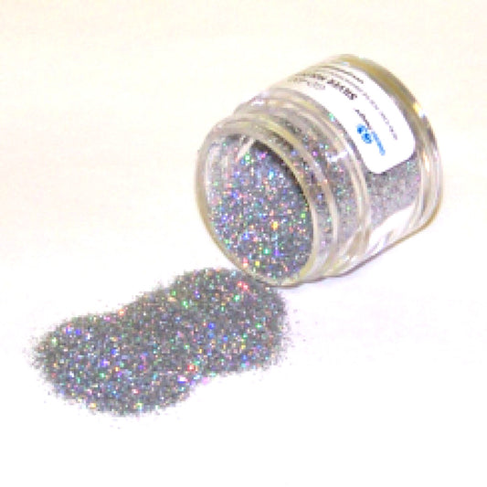 Small clear jar tipped on its side spilling silver hologram glitter dust onto a white surface, with fine sparkling particles reflecting rainbow highlights.