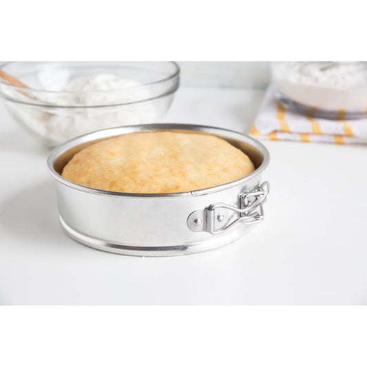 Baked cake resting in a 6-inch springform pan on a kitchen counter with mixing bowls in the background.