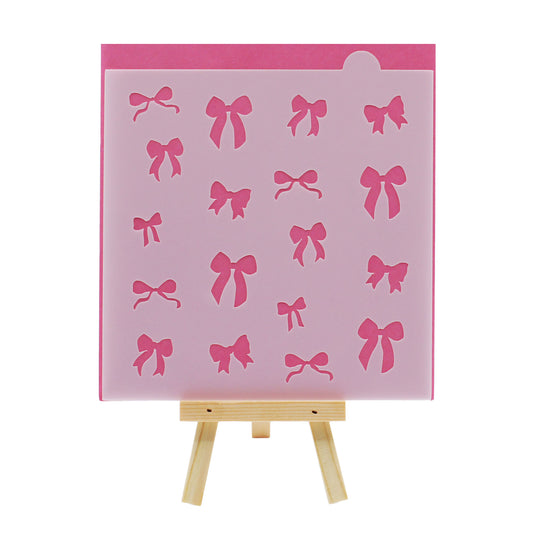 Small assorted bow cookie stencil with multiple ribbon bow cutouts in different shapes and sizes, displayed in translucent plastic against a pink background on a small wooden easel.