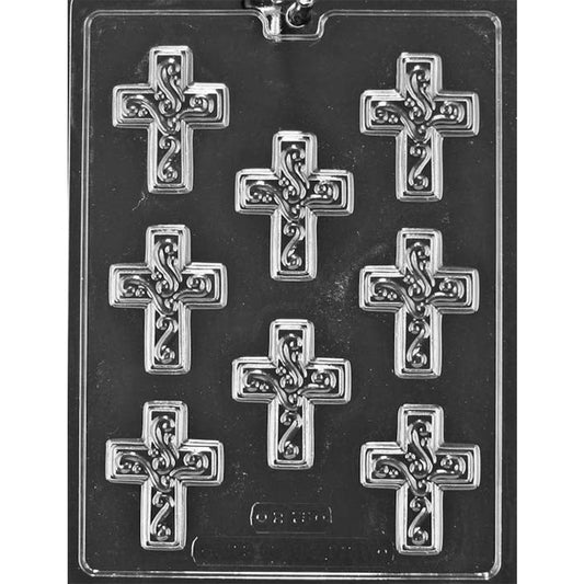 Clear chocolate mold with eight small cross-shaped cavities featuring raised swirling scrollwork and decorative flourishes on a dark background.