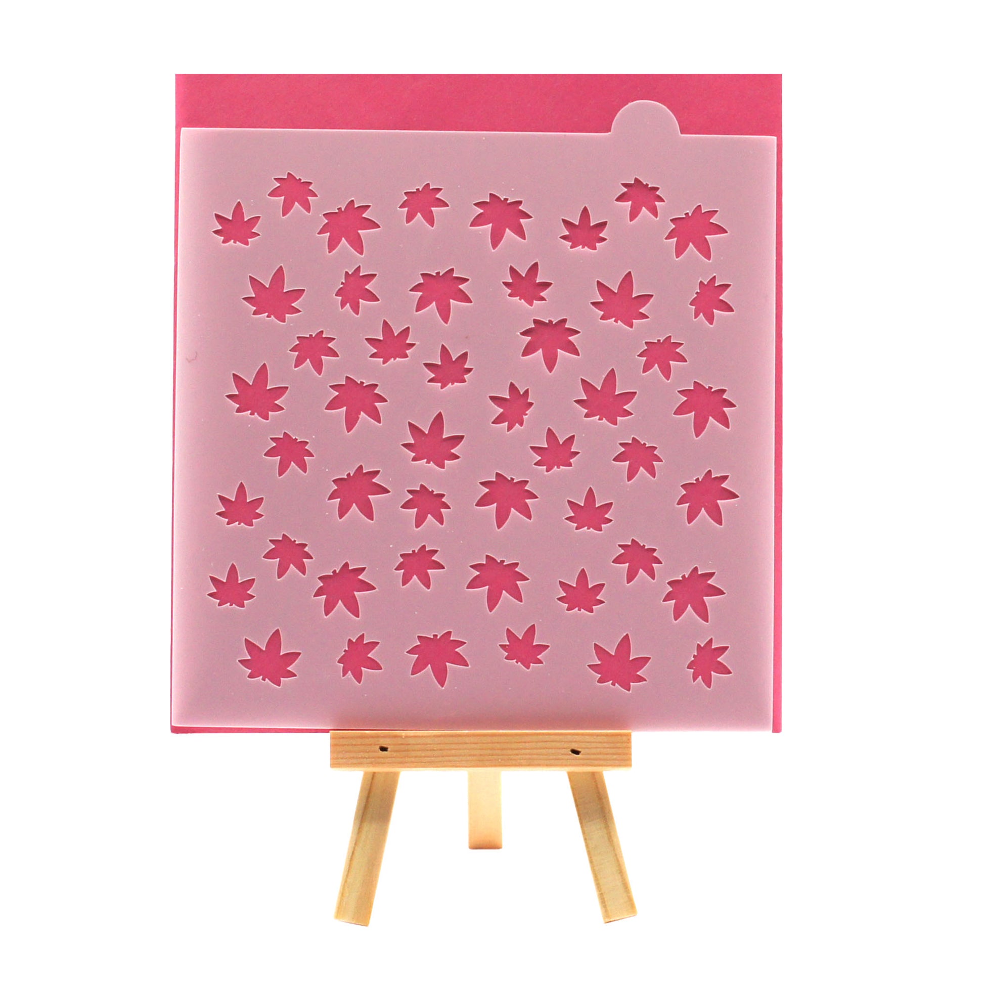 Small marijuana leaf pattern cookie stencil on a pink background, shown on a small wooden easel.