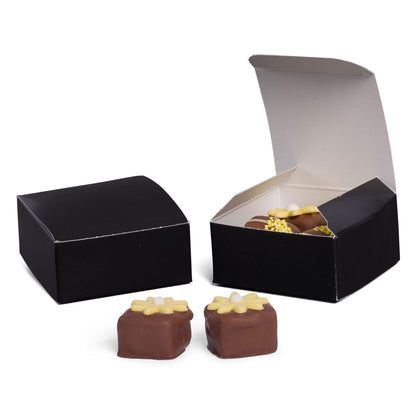 Two small black square truffle boxes, one open with chocolates inside, with two chocolate truffles in front on a white background.