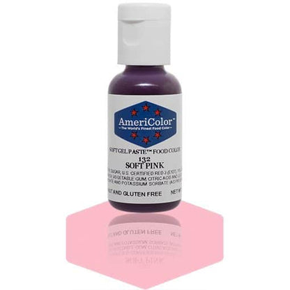 A bottle of AmeriColor Soft Pink soft gel paste food coloring with a white cap and blue label featuring red stars, standing on a pale pink reflective surface that mirrors the bottle.