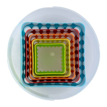 Top-down view of nested square cookie cutters inside a clear round container, showing the layered colors and fluted scallop edges.