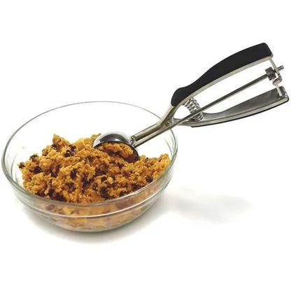 Stainless steel 3-tablespoon cookie scoop resting in a glass bowl filled with chocolate chip cookie dough.