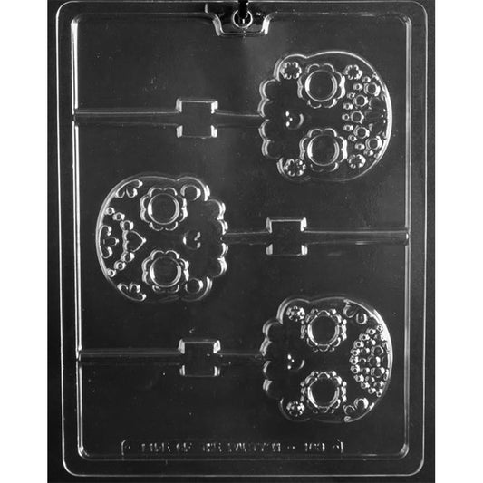 Clear plastic sugar skull chocolate lollipop mold with three 2 3/4-inch cavities featuring floral eyes, dotted forehead patterns, scrollwork, and scalloped teeth.