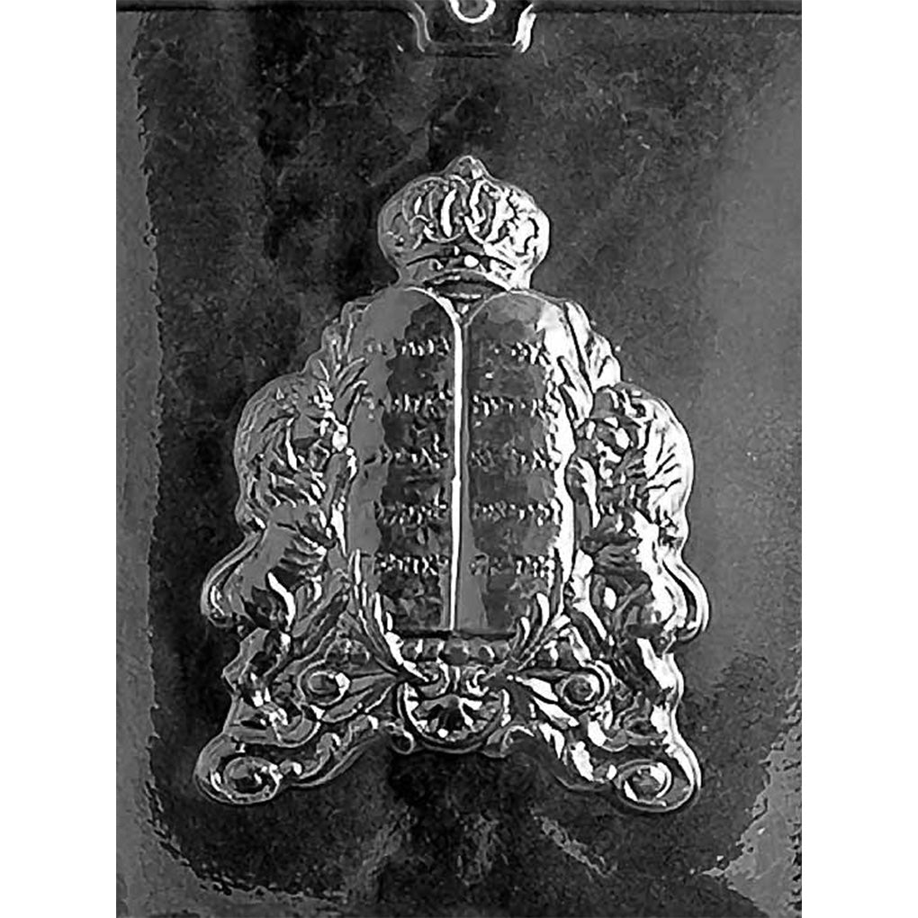 Clear plastic chocolate mold photographed on a black background with one large cavity shaped like two stone tablets with Hebrew lettering, topped with a crown and flanked by two lions.