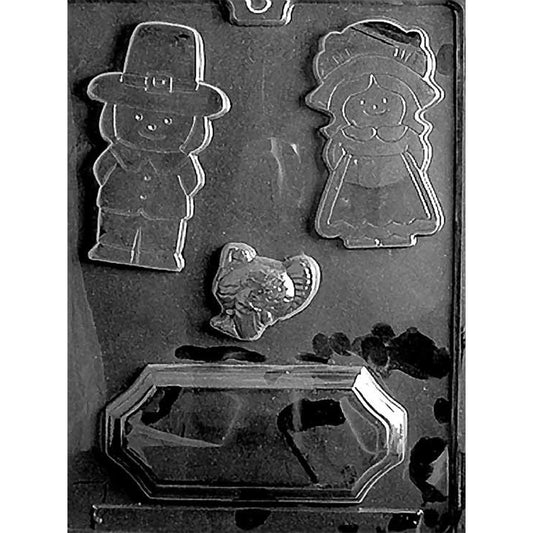 Clear chocolate mold with four Thanksgiving-themed cavities featuring a pilgrim man, pilgrim woman, small turkey, and a large base for creating an edible holiday centerpiece.