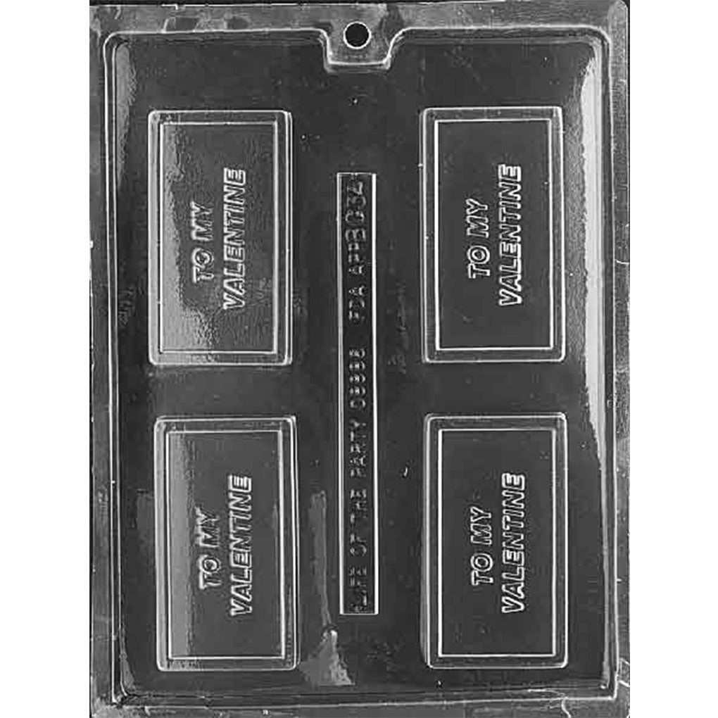 Clear plastic chocolate bar mold photographed on a dark background with four rectangular cavities, each featuring raised “TO MY VALENTINE” lettering inside a bordered frame.