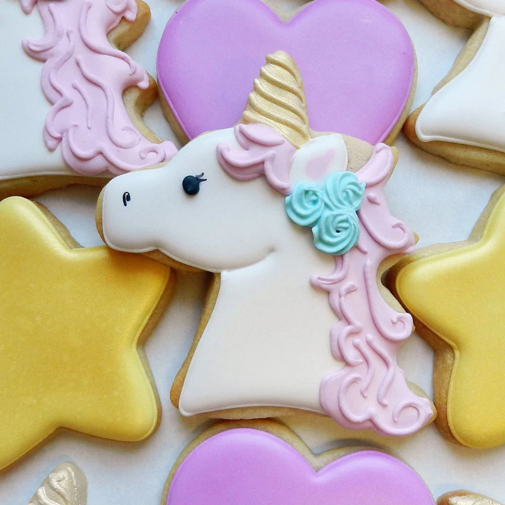 Unicorn sugar cookie with white icing, a pink mane, a golden horn, and blue floral details, surrounded by heart and star cookies.