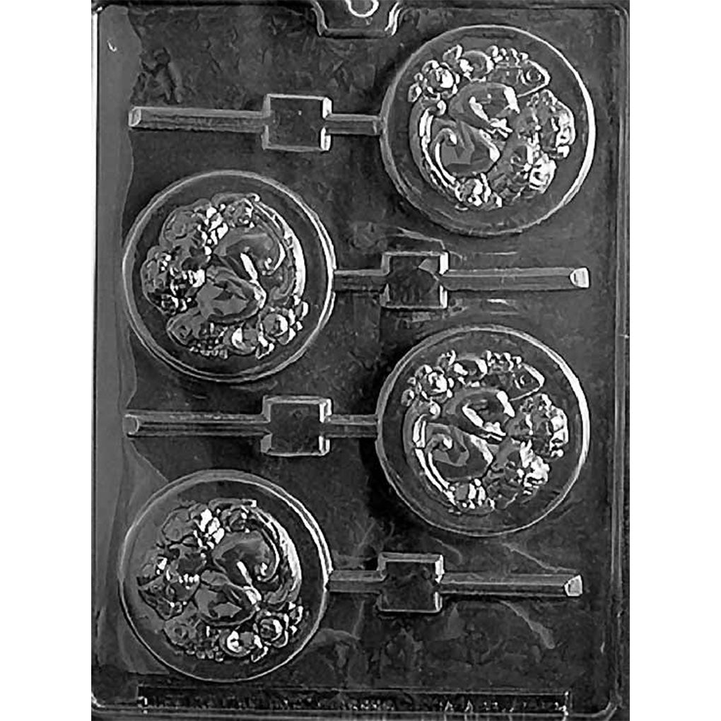 Clear plastic chocolate mold with four round medallion cavities showing two cherubs embracing, one kissing the other on the cheek, surrounded by ornate floral and scrollwork details on a dark background.