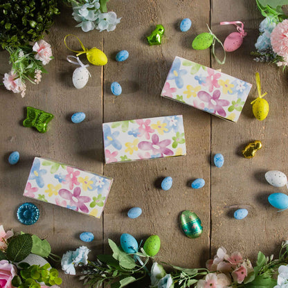 Watercolor daisy candy boxes arranged on a rustic wood surface with spring flowers and decorative Easter eggs.
