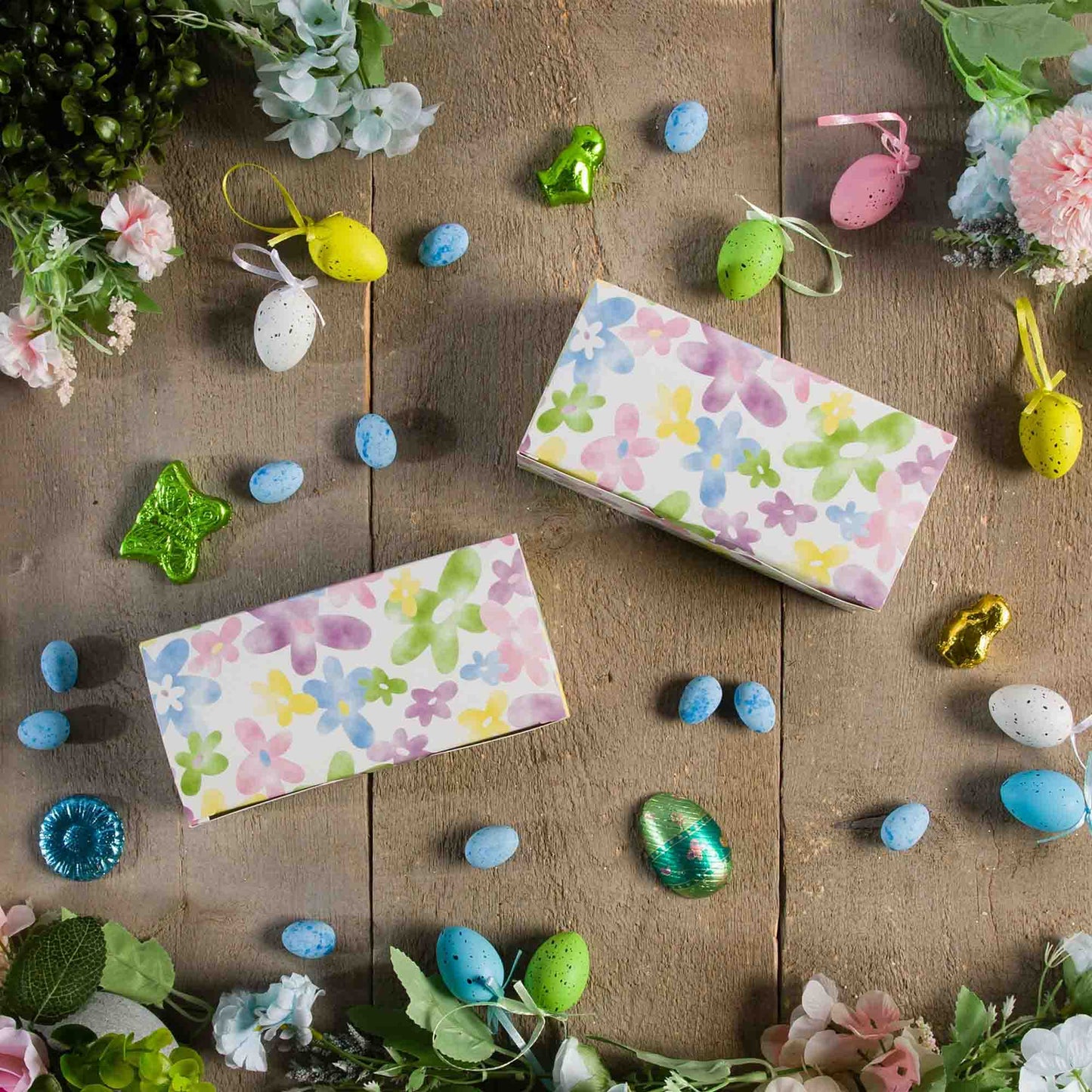 Watercolor daisy candy boxes styled on a rustic wood surface with spring florals and decorative Easter eggs.