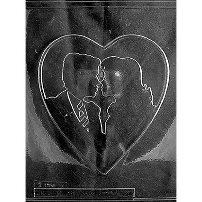 Clear plastic chocolate mold photographed against a black background featuring a large heart cavity with a bride and groom silhouette facing one another inside the heart.
