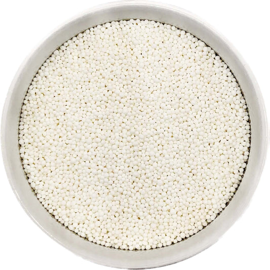 Bowl of bright white nonpareil sprinkles on a white background.