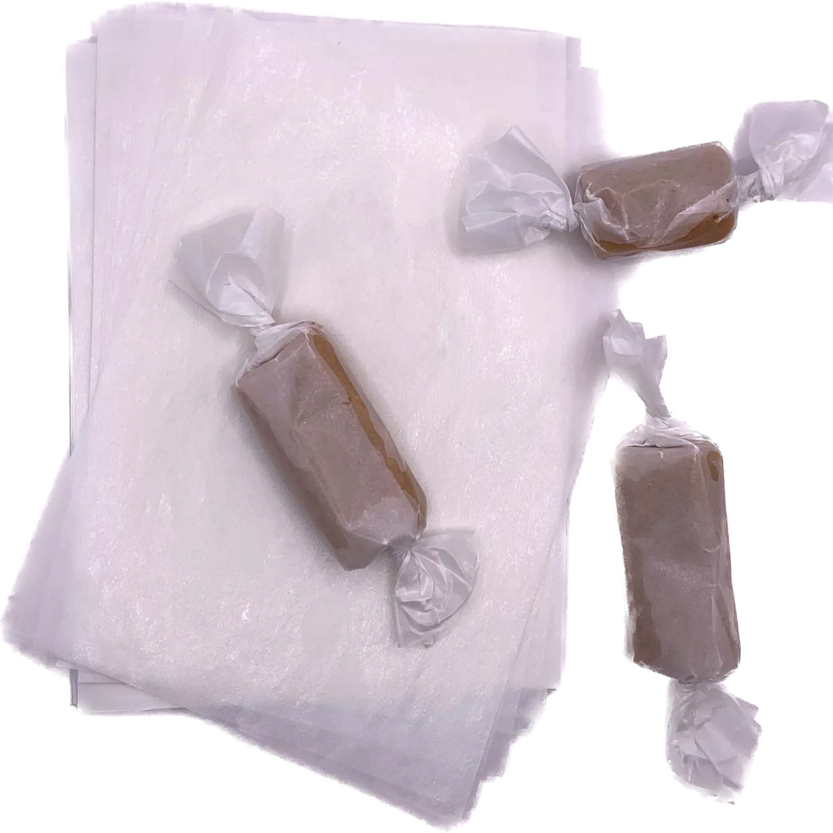 Stack of white 4" x 5" wax caramel wrappers with three rectangular caramel pieces individually wrapped and twisted at both ends.