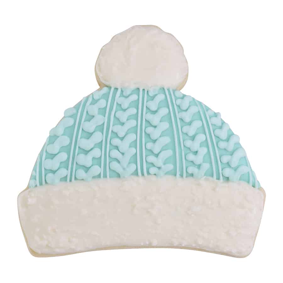 Decorated sugar cookie in the shape of a winter hat with textured blue icing and a fluffy white brim and pom-pom.