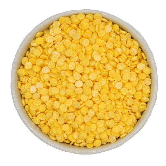 White bowl filled with small round pearl yellow confetti quin sprinkles with a soft shimmery finish.