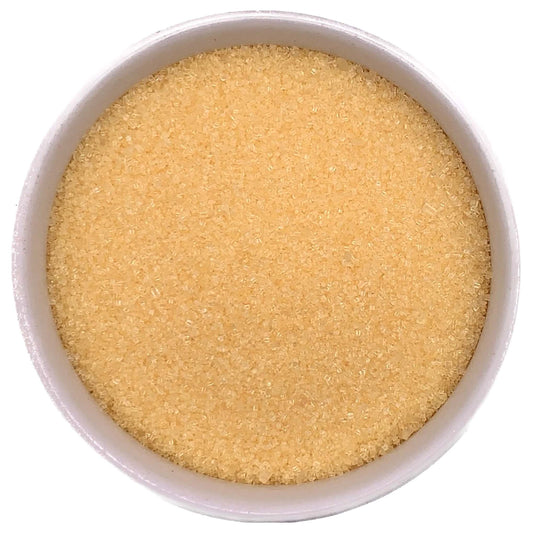 Top-down view of a white bowl filled with yellow fine sanding sugar, showing tiny golden-yellow crystals with a soft, shimmering texture.
