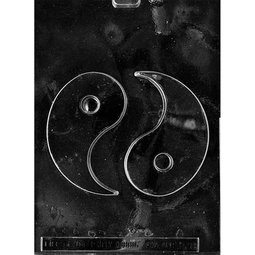 Clear plastic chocolate mold featuring a yin-yang symbol with two interlocking curved halves and a small raised dot in each half, photographed on a dark background.