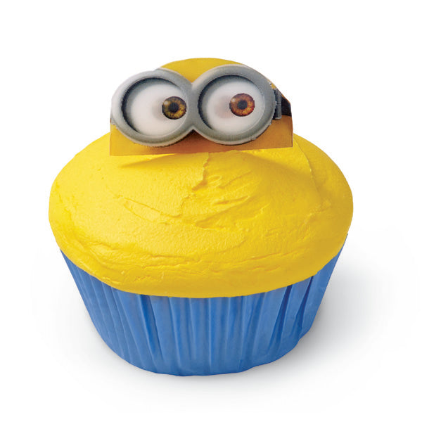 Cupcake with bright yellow icing in a blue cup, topped with a Minion's face wearing its characteristic goggles from 'Despicable Me'.