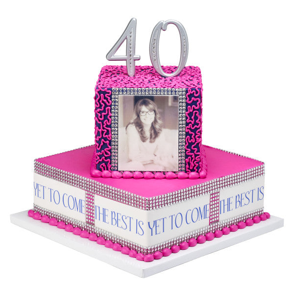 Bright pink milestone celebration cake with a silver photo frame topper displaying a personal picture, surrounded by the message 'The best is yet to come', suitable for memorable birthday or anniversary parties.