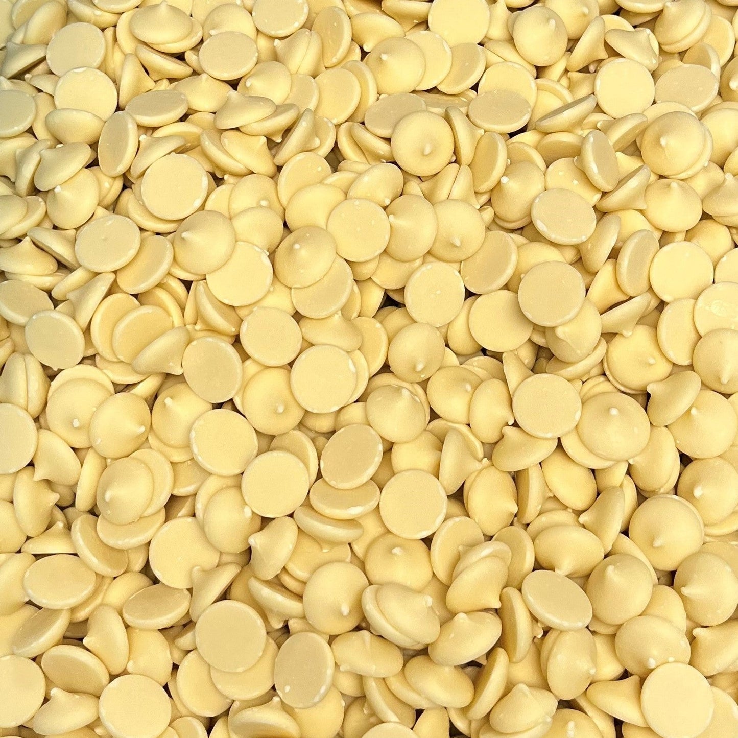 Close-up overhead view of a large batch of creamy white chocolate wafers with uniform shape and soft vanilla coloring, highlighting texture and shine.