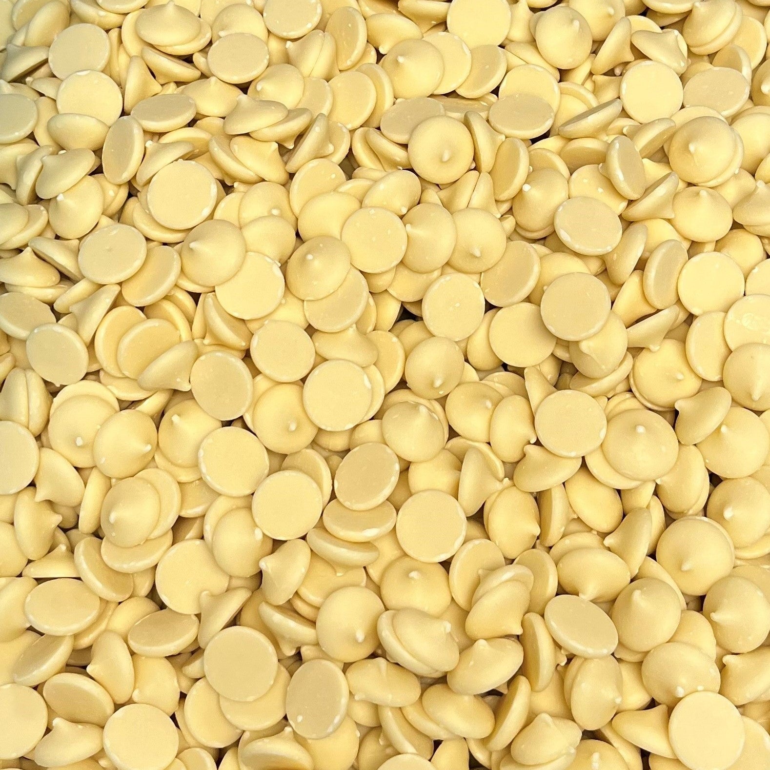 Close-up overhead view of a large batch of creamy white chocolate wafers with uniform shape and soft vanilla coloring, highlighting texture and shine.