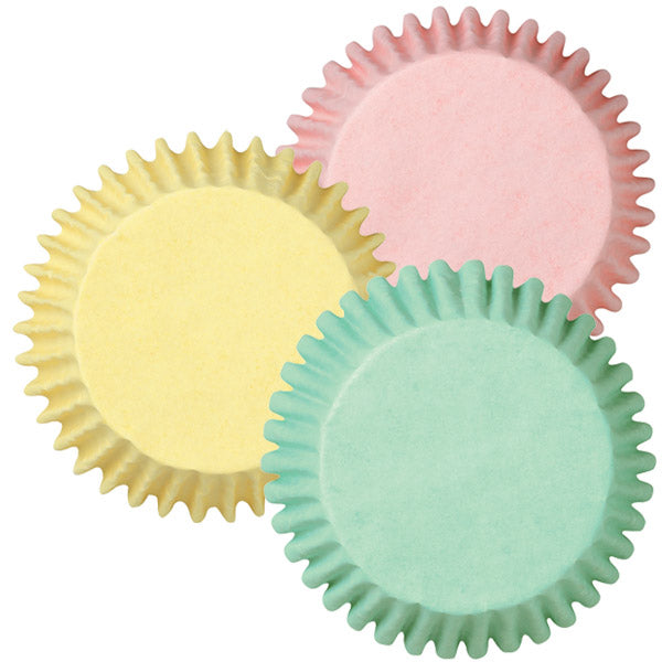 Top view of Wilton pastel baking cups in yellow, mint green, and pink, fanned out against a white background.